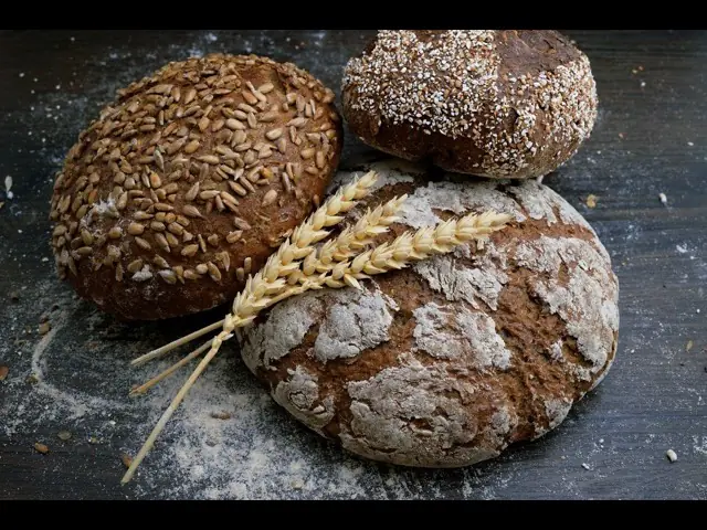 Trois miches aux graines et farinées qui refroidissent sur une surface foncée.