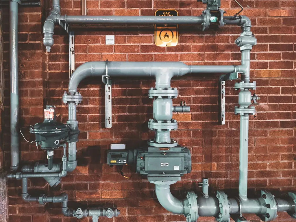 Des tuyaux d'alimentation et des valves en métal gris montés sur un mur de brique rouge.